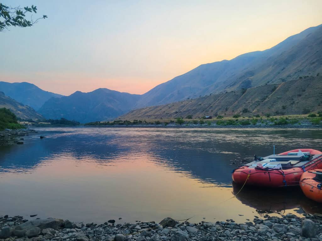Sunset view of the Snake River in Hells Canyon with rafting boats along the shoreline during a whitewater rafting adventure with Tributary Whitewater.